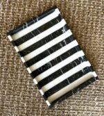 Siyah beyaz yatay çizgili modern mermer sunum tepsisi, kahverengi bir halı üzerinde yer alıyor.