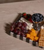 . Siyah beyaz çizgili modern mermer tepside peynir, üzüm, kraker ve meyveler yer alıyor.