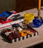 . Siyah beyaz çizgili modern mermer tepside peynir, üzüm, kraker ve meyveler yer alıyor.