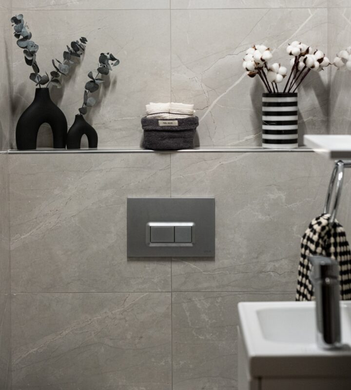 Lavabo, tuvalet ve üzerinde siyah beyaz çizgili vazo bulunan rafın yer aldığı modern bir banyo.