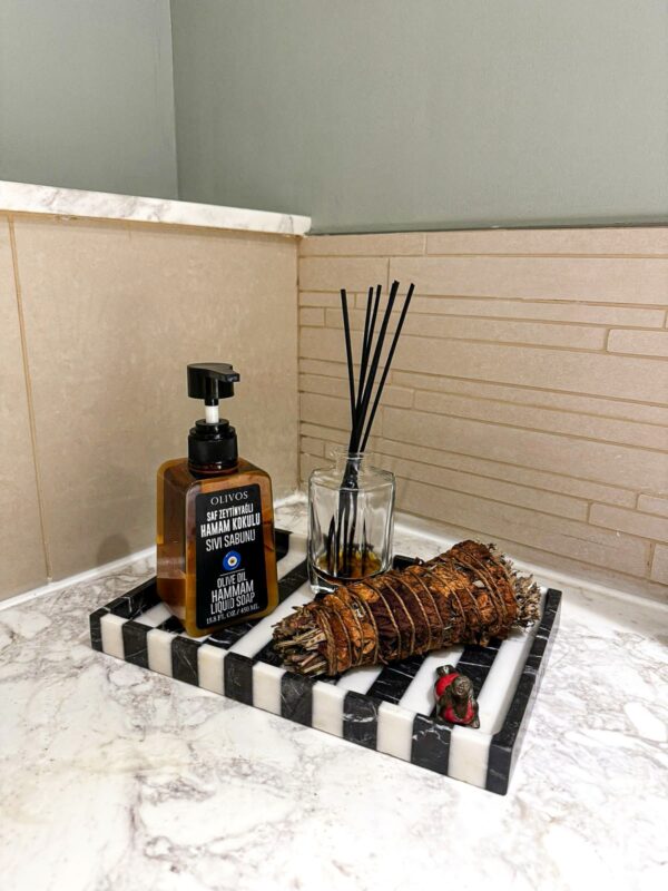 Mermer bir tepsi üzerinde parfüm şişesi ve bir mum, küçük banyo dekorasyonuna doğal bir dokunuş katıyor.