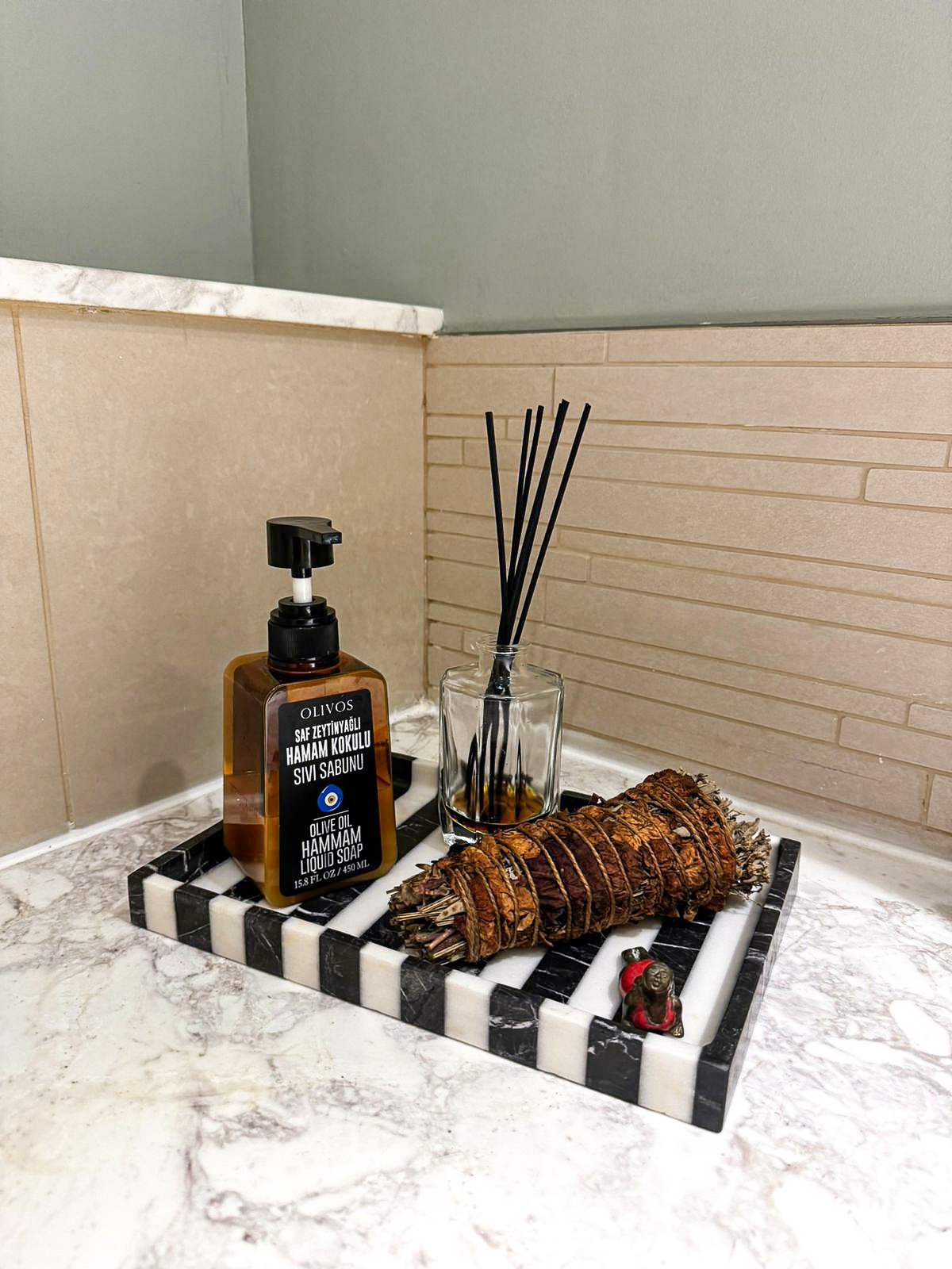 Mermer bir tepsi üzerinde parfüm şişesi ve bir mum, küçük banyo dekorasyonuna doğal bir dokunuş katıyor.